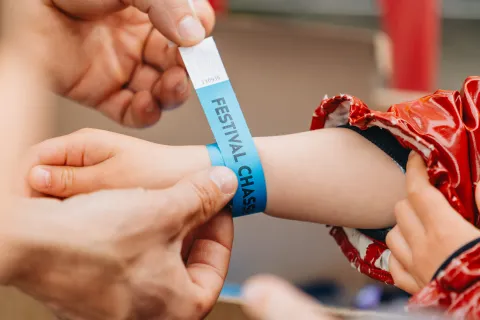 Pose d’un bracelet bleu « Festival Chasseurs d’Orages » au poignet d’un enfant.