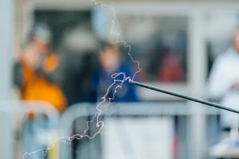 Arc électrique au bout d’une tige métallique, spectateurs flous en arrière-plan.