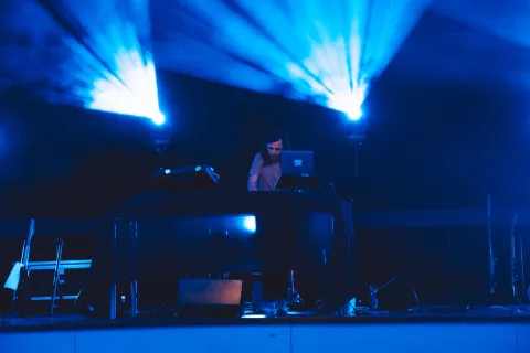 Concert électronique : musicien derrière son ordinateur sous des faisceaux bleus.