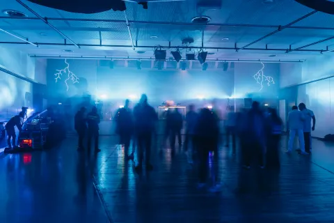 Grande salle baignée de lumière bleue, éclairs dessinés aux murs, visiteurs en mouvement.