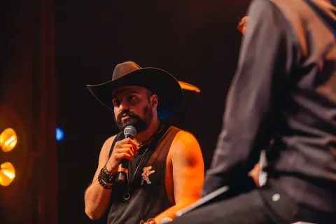 Intervenant au chapeau de cow-boy, micro en main, dans une lumière chaude.