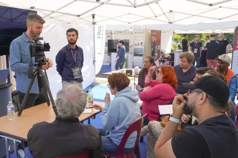 Interview filmée sous une tente, devant des visiteurs attentifs.