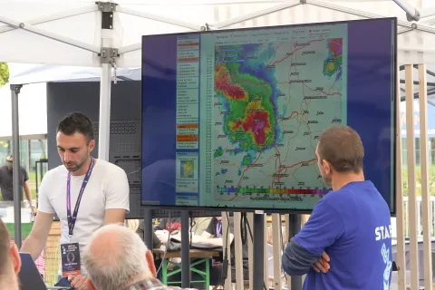 Deux personnes commentent une image radar d’orage sur un grand écran, sous une tente.