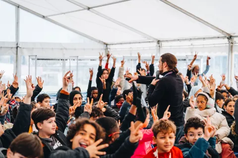 Matinée des scolaires : des dizaines d’élèves lèvent la main pour répondre à un animateur, sous la tente.