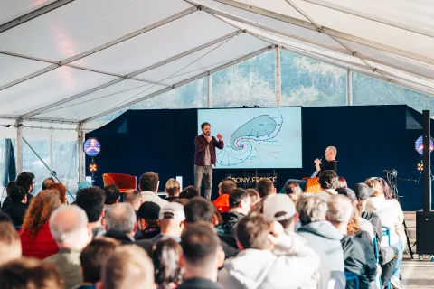 Conférence sous la tente devant un public assis, schéma d’un cyclone projeté sur l’écran.