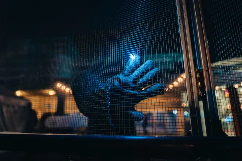 Main gantée tendue vers un arc électrique derrière une grille, la nuit.