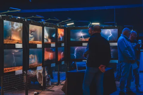 Visiteurs devant une exposition de grands tirages d’orages et d’éclairs, dans une lumière bleue.