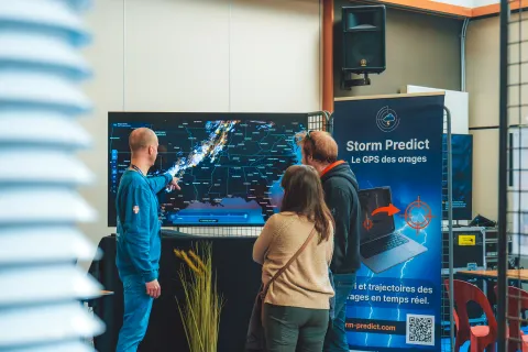 Stand Storm Predict : un exposant montre une carte des orages en temps réel à deux visiteurs.