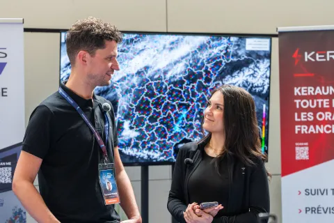 Stand Keraunos : un exposant échange avec une visiteuse devant une carte des impacts de foudre.