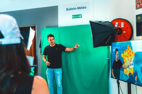 Atelier Bulletin météo : un visiteur présente la météo devant un fond vert, son image incrustée sur l’écran.