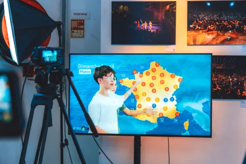 Atelier Bulletin météo : un enfant présente la carte de France sur l’écran de contrôle, derrière la caméra.