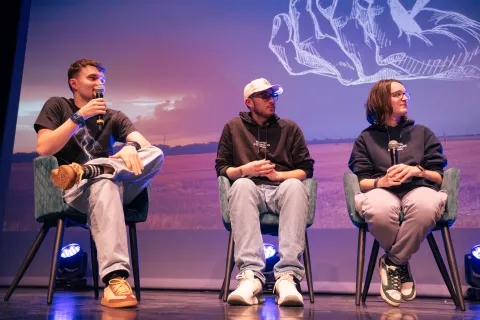 Trois intervenants assis sur scène, micro en main, pendant une discussion.
